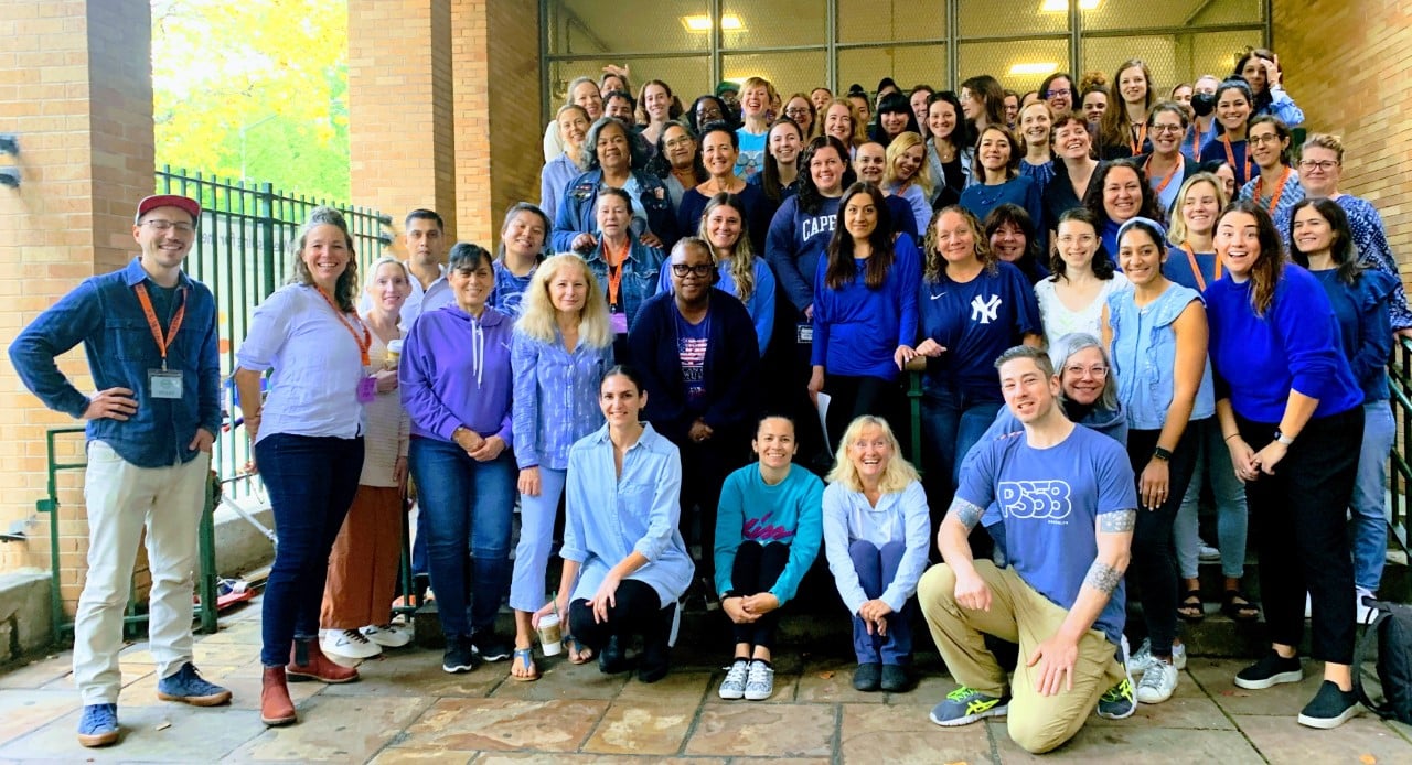 group image of staff wearing blue standing in front of main entrance of school