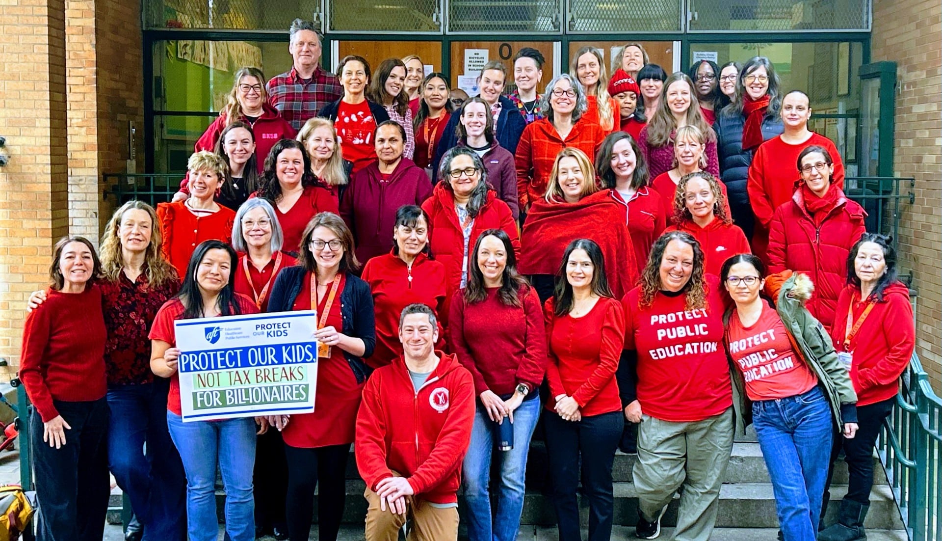 PS 58 staff members wearing in a group portrait on the steps of the main entrance.